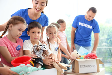Happy volunteers with children sorting donation goods indoors
