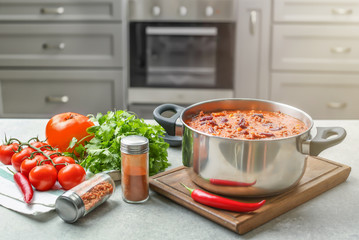 Saucepan with delicious chili con carne on wooden board