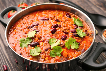 Saucepan with delicious chili con carne on table