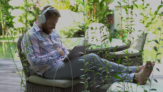 Man relaxing in the garden and watching something funny on modern notebook
