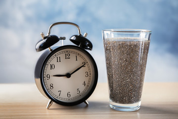 Glass of water with chia seeds and alarm clock on table