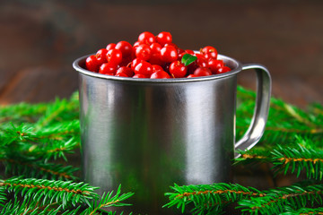 Cowberry, foxberry, cranberry, lingonberry in an aluminum mug on a brown wooden table. Surrounded by fir branches.