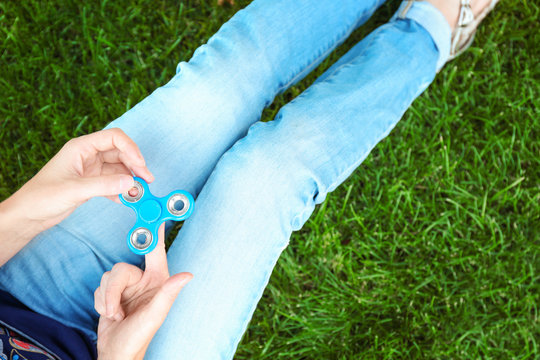 Woman rolling spinner while sitting on green grass outdoors