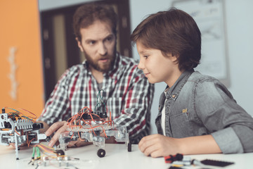 A man helps a boy with a robot assembly. The boy looks carefully as a man collects a robot