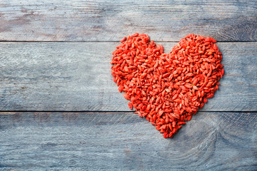 Goji berries in shape of heart on wooden table. Heart health concept