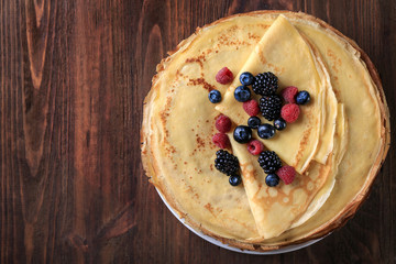 Stack of delicious thin pancakes with berries on plate against wooden background