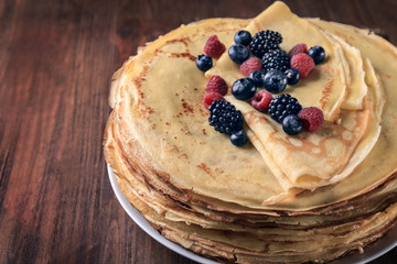 Plate with delicious thin pancakes and berries on wooden background