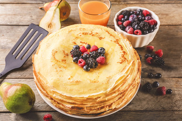 Plate with delicious thin pancakes and berries on wooden background