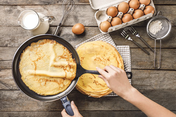 Woman making thin pancakes on frying pan in kitchen