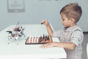 A little boy is playing chess with a gray robot. Robot plays for whites
