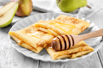 Plate with delicious thin pancakes on wooden background