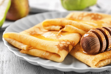 Delicious thin pancakes served with honey on plate, closeup