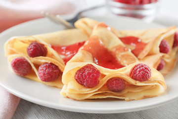 Delicious thin pancakes served with raspberries and jam on plate, closeup