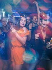 Happy friends dance in motion. Joyful New Year company in night club, active Christmas celebration. Disco party in blurred colors, modern youth life - obrazy, fototapety, plakaty