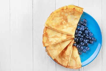 Delicious thin pancakes served with blueberries on plate against wooden background