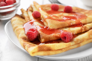 Delicious thin pancakes served with raspberries and jam on plate, closeup