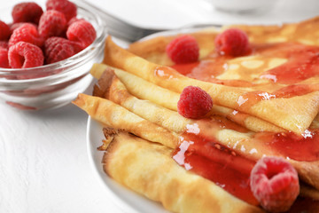 Delicious thin pancakes served with raspberries and jam on plate, closeup