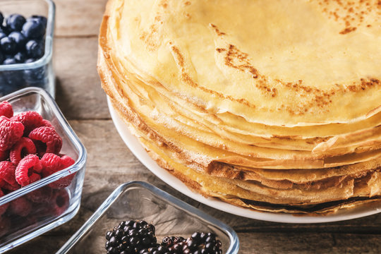 Stack of delicious thin pancakes on plate served with berries, closeup