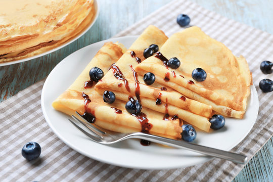 Delicious thin pancakes served with blueberries and jam on plate
