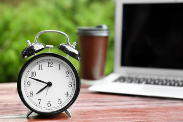 Clock alarm on wooden table outdoors. Morning routine concept