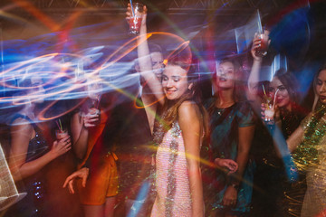 New Year party at night club in blurred motion. Joyful friends with cocktails at Christmas...
