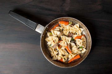 Flat lay photo of a fresh cooked pasta with mushrooms and vegetables in a pan on dark concrete table, horizontal imagen,flatlay image