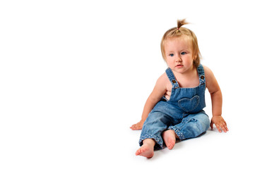 Cute little baby girl in jeans overalls sitting on white background, isolated