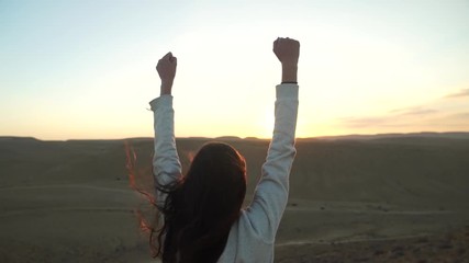 Young woman lifting her arms in  a desert sunset - reaching her goal