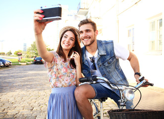 Happy couple on scooter making selfie photo on smartphone outdoors.