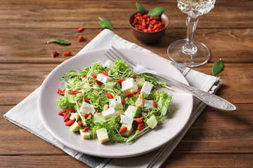 Plate with delicious goji berry salad on wooden background