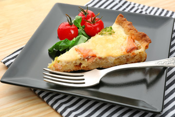 Plate with piece of salmon quiche pie on table