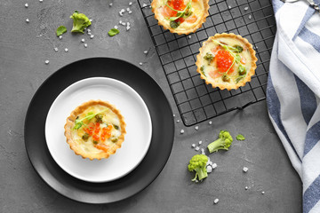 Plates and baking grid with tasty salmon tartlets on table