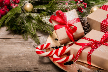 Christmas concept, wooden table with pine tree branches and gift present boxes with red satin polka dot ribbons, red berries on golden tray, candy canes, ornaments, table top decoration, copy space