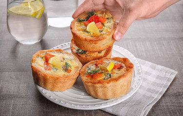 Woman putting tasty salmon tartlets on plate