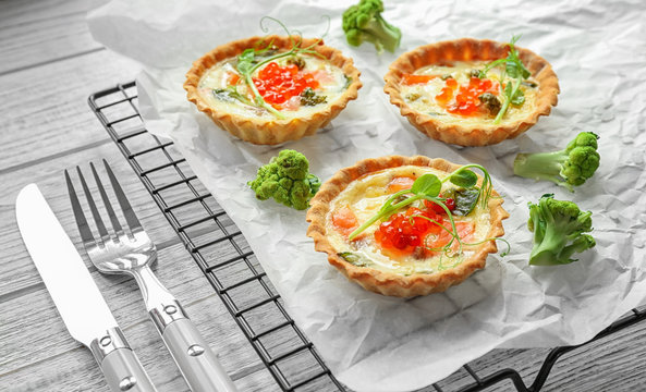 Baking grid with tasty salmon tartlets on table