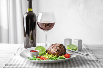 Plate with juicy steak and glass of wine on table against light background