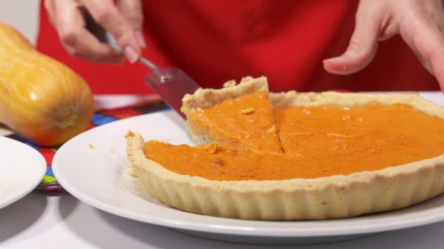Making homemade pumpkin pie with fresh pumpkin. Thanksgiving sweet dessert recipe. Woman cuts a piece of pie and puts it on a plate. Panning right to left.