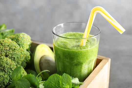 Glass with green smoothie and products in wooden basket on grey background