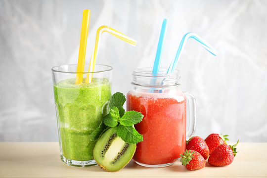 Glassware with delicious kiwi and strawberry smoothies on table against light background