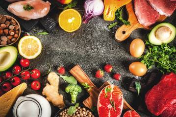Healthy diet background. Organic food ingredients, superfoods: beef and pork meat, chicken filet, salmon fish, beans, nuts, milk, eggs, fruits, vegetables. Black stone table, copy space top view