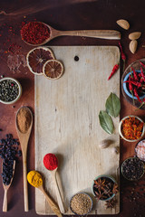 Various indian spices in wooden spoons, seeds, herbs and nuts and empty wooden board