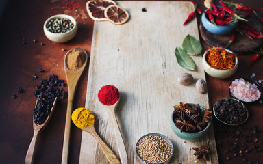Various indian spices in wooden spoons, seeds, herbs and nuts and empty wooden board