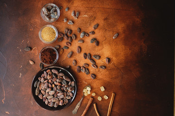 Raw cocoa beans, cacao powder and brown sugar on dark stone background