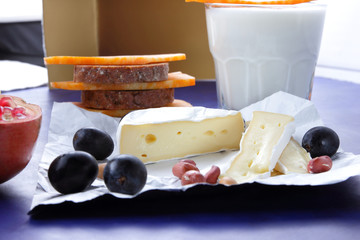 Camembert cheese, orange marble cheese, a glass of milk, pomegranate, olives, peanut grains, dark...