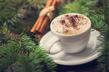 A cup of coffee with the branches of the Christmas tree on a wooden table