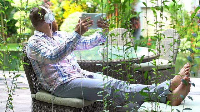 Man looks happy while sitting in the garden and having a videocall on tablet

