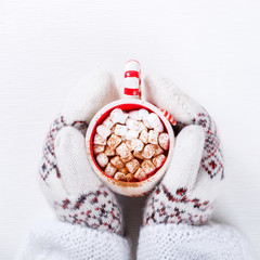 Female hands holding hot chocolate with marshmallow and cinnamon. Warming holiday drink on a white...