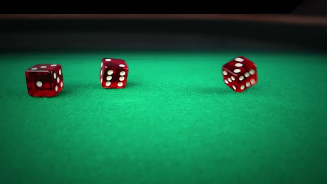three red dice rolling on green game gambling table on black background, shooting with slow motion, concept of sport recreation leisure game in the casino