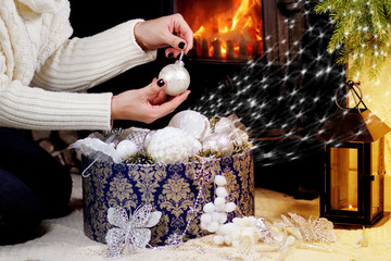 девушка возле камина достает елочные украшения из...