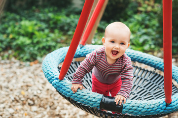 Baby girl having fun in the park, 9-12 months old kid playing in the big swing, summer playground, activities for children